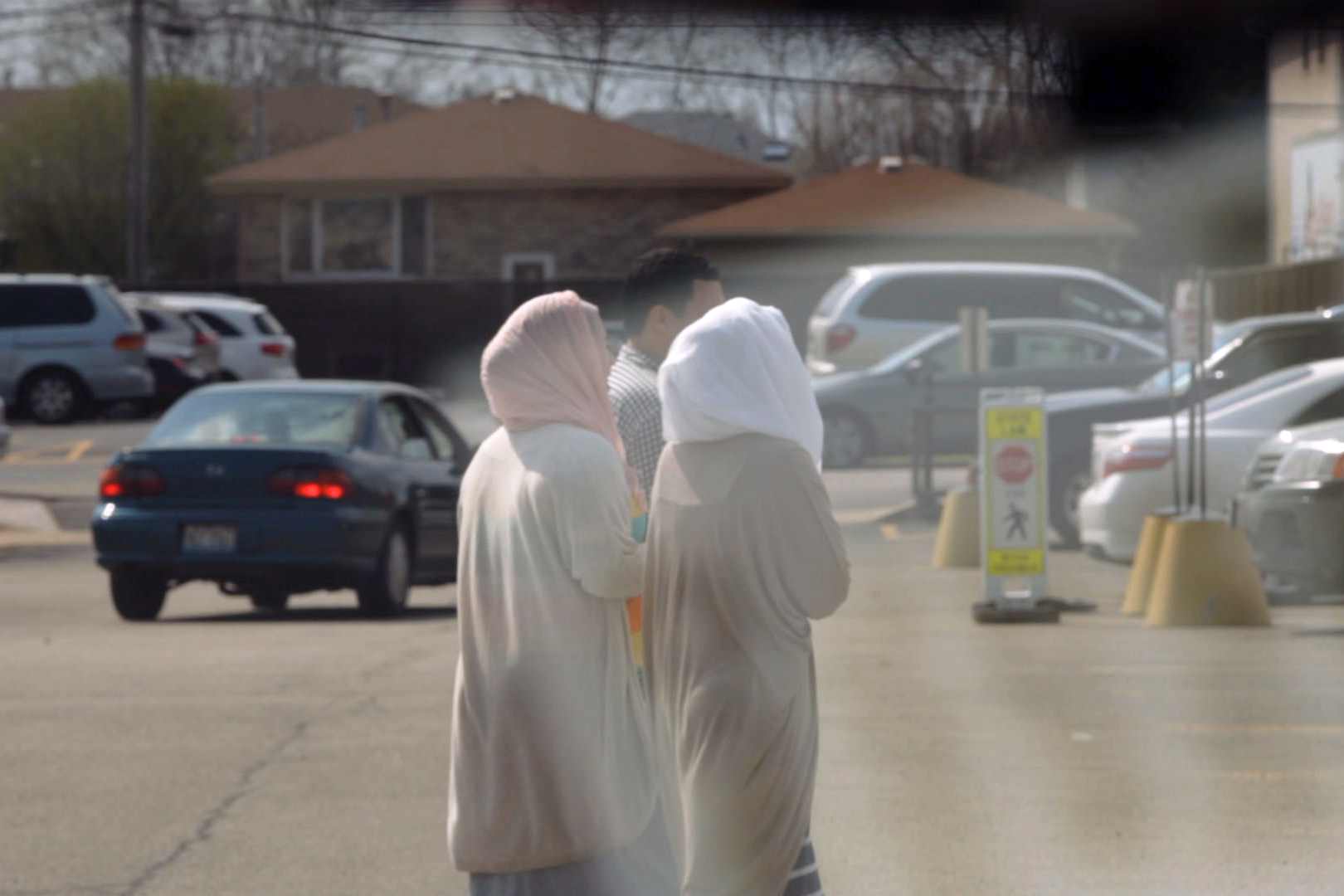 stillshot from the documentary featuring three people, two in hijab, and one man with short hair walking. the image is murky and taken from a distance, suggesting that it was taken from within a car